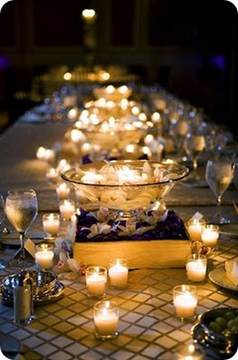 Votives placed casually around raised centerpieces consisting of floating candles in glass bowls.