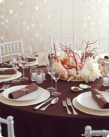 Assortment of large shells and painted manzanita branches to resemble coral surround a hurricane with a bright white candle